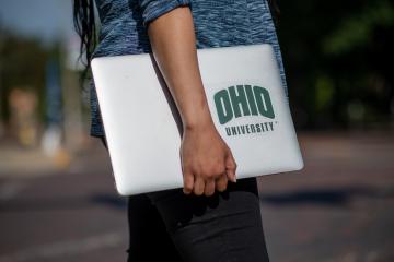 Person outside holding laptop in right arm.