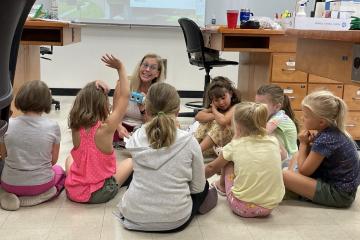 Jenni Domo sits on the floor with a group of kids