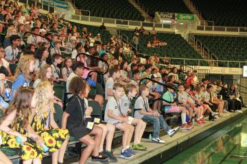 A large audience made up of children sit in bleachers