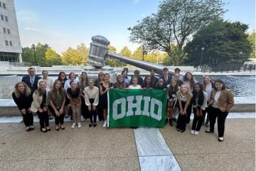 A group of high school students pose in front of a fountain with a giant gavel sculpture