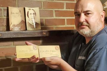 Image of Chris Sauders holding letters in front of two photos on mantle