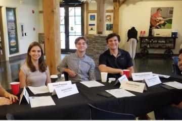 A group of students are seated at a conference table, smiling at the camera