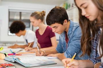 Four children sitting at a desk writing notes and reading textbooks.