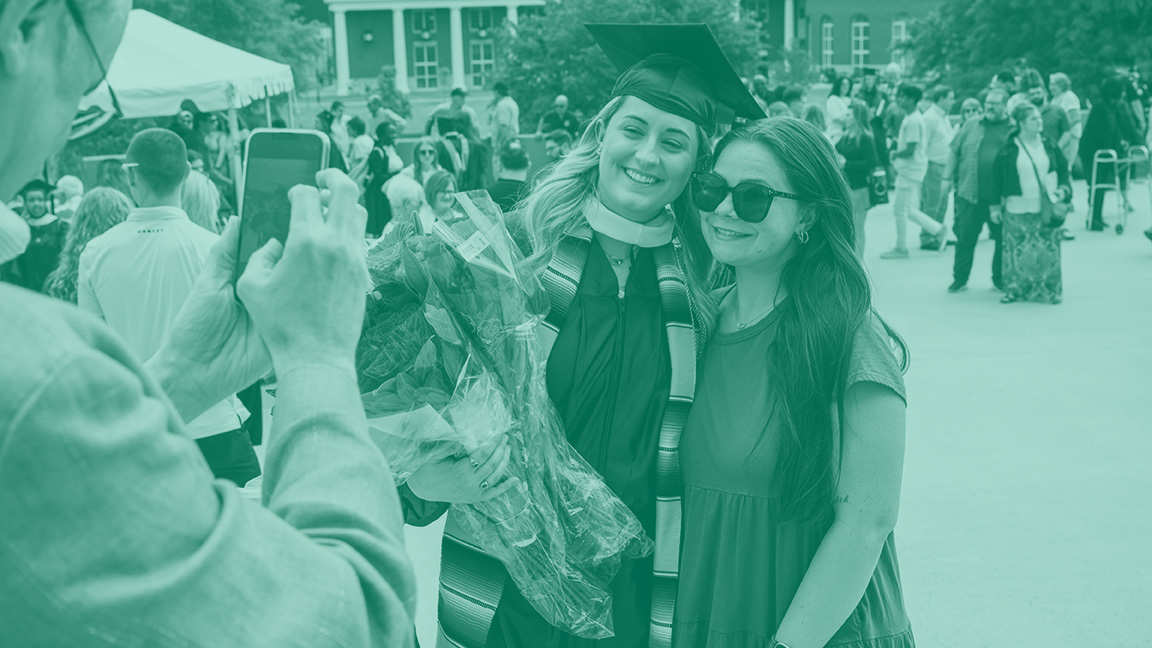 graduating student, still wearing cap and gown, poses for a photo with her mom.