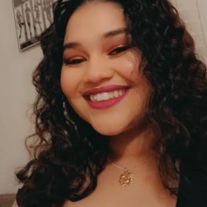 Alisha Rivera Aquino smiles in a selfie photo, wearing a black tank top and a necklace with a gold charm