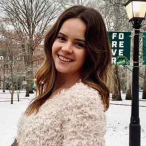 Landy Price stands in the snow on campus and smiles while wearing a fuzzy sweater.