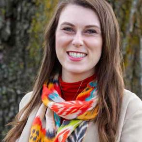 Shannon Hamelund smiles and wears a red turtleneck and white blazer with a colorful scarf