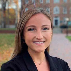 Tessa Corio stands on college green smiling and wearing a black blazer
