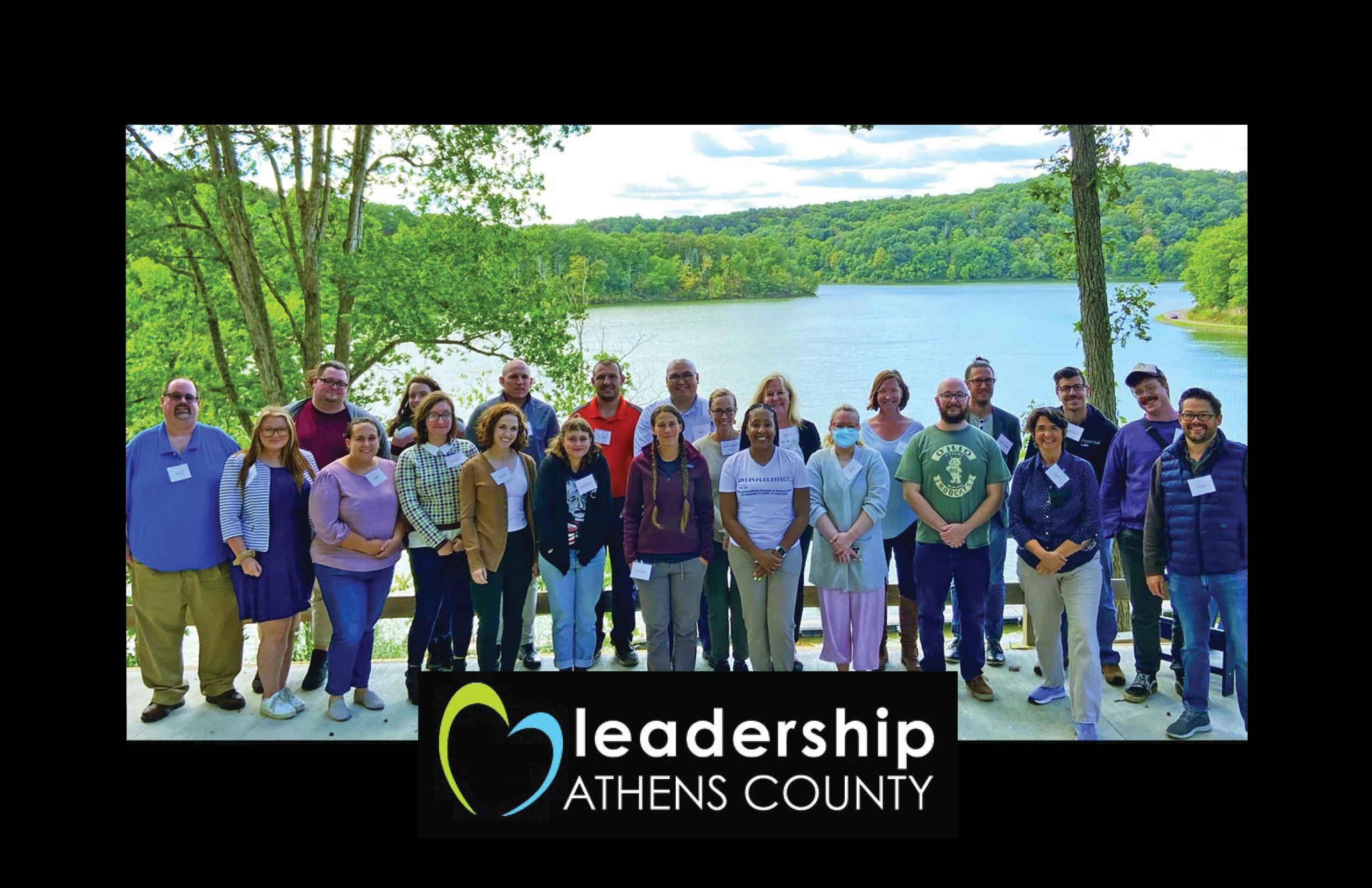 A large group photo standing infront of a lake surrounded by trees. Logo of "Leadership Athens County" is layered at the bottom of image.